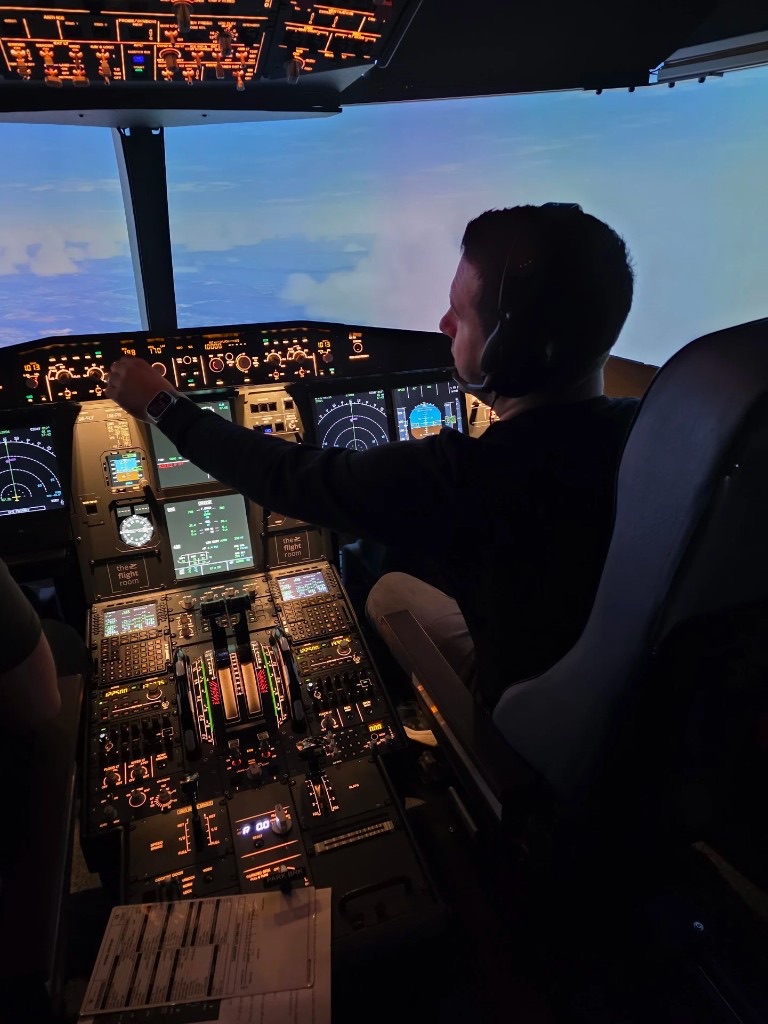 Pilot sa slušalicama za komandama A320 kokpita, pogled preko ramena na instrumente i nebo